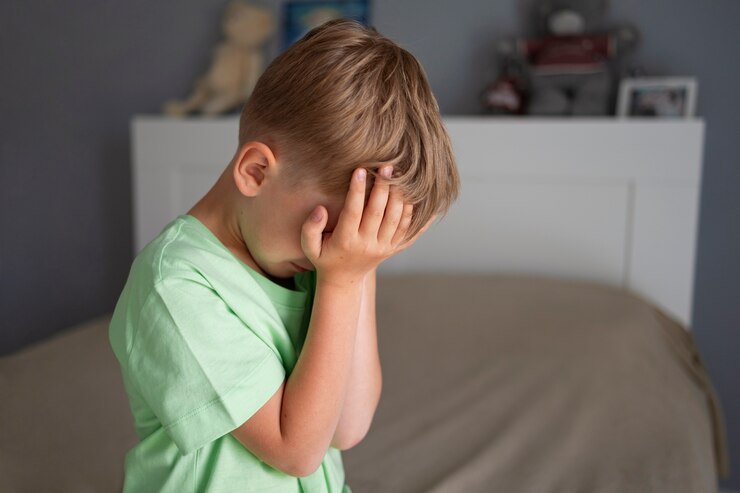 Menino cobrindo o rosto com as mãos, indicando desconforto por dor de cabeça.