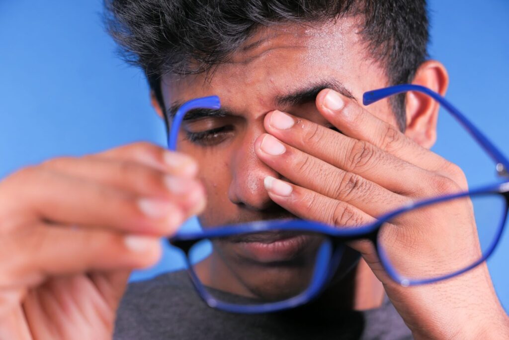 Homem removendo os óculos e esfregando os olhos, ilustrando desconforto visual causado pela síndrome de Irlen.