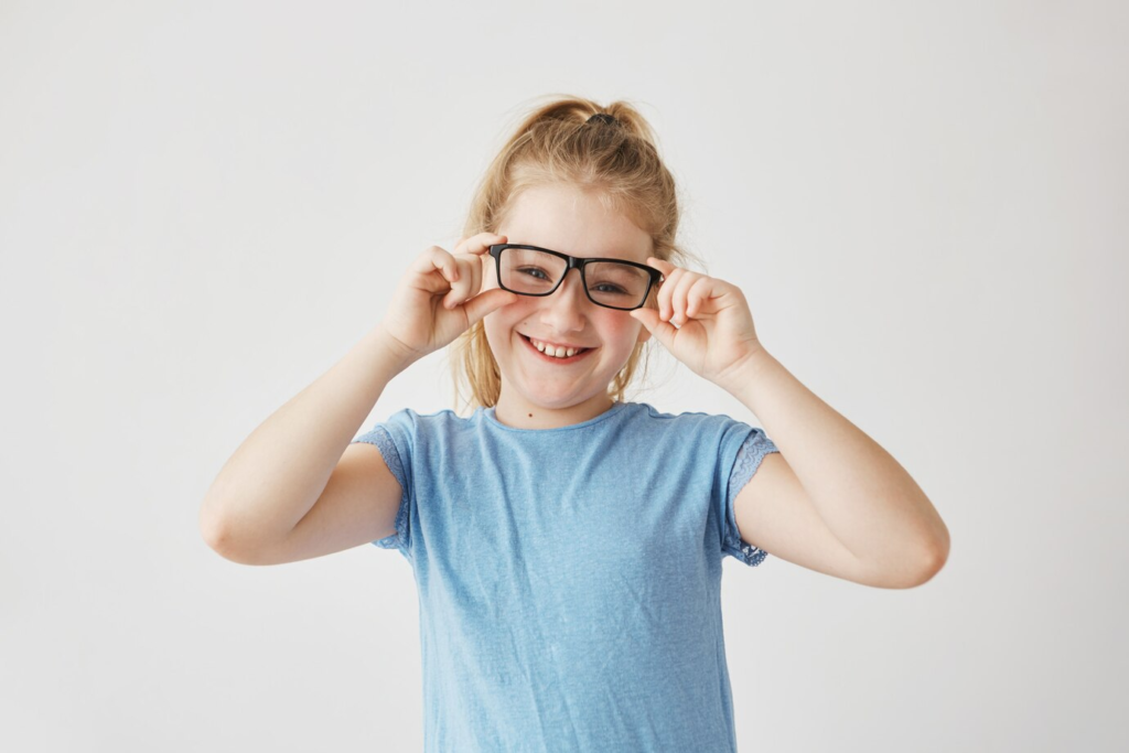 Menina sorridente ajustando óculos - astigmatismo em crianças.