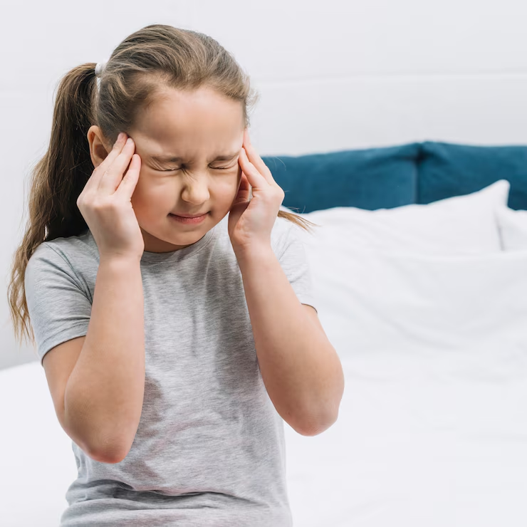 Menina com as mãos na cabeça, expressão de incômodo por dor de cabeça.